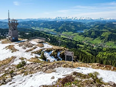 KI-generiertes Symbolbild: Gipfelplateau mit Restschnee, Aussichtsturm und Alpen am Horizont